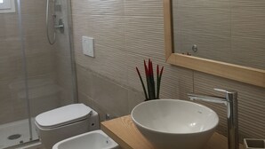 Un baño moderno con ducha de vidrio, lavamanos blanco y encimera de madera, y un espejo grande.