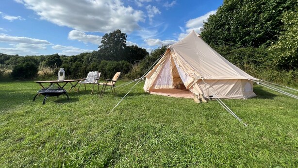 Ein Zelt auf einer grünen Wiese, mit zwei Stühlen und einer Laterne in der Nähe.