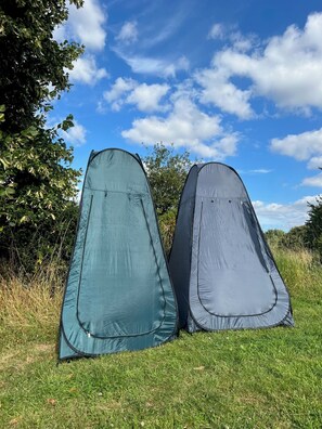 Deux tentes sont installées dans un champ herbeux, avec des arbres et un ciel dégagé en arrière-plan.