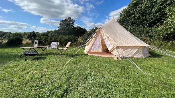 Ein Zelt auf einer grünen Wiese, mit zwei Stühlen und einer Laterne in der Nähe.