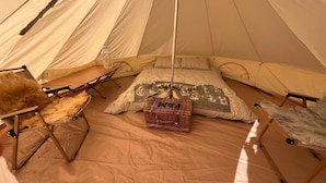 Ein Zelt mit Bett, Kissen, Decke, einem Korbwäschekorb und einem Klappstuhl.