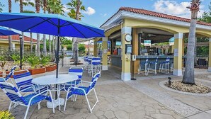 An outdoor patio area with tables and blue chairs, a covered seating area, and a clock on the wall. - Disney Vila, Near Parks, Private Pool & Arcade (Kissimmee)