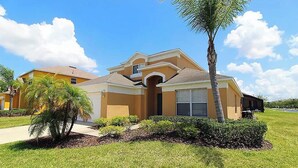 A residential house with a brown facade, a central entrance, and a small front yard with a palm tree and shrubs. - Disney Vila, Near Parks, Private Pool & Arcade (Kissimmee)