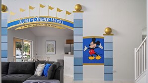 A living room with a grey sectional sofa, a framed picture on the wall, and a Mickey Mouse mural on the wall. - Disney Vila, Near Parks, Private Pool & Arcade (Kissimmee)