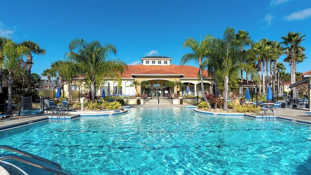 A swimming pool with clear blue water, surrounded by palm trees and a building with a red-tiled roof. - Disney Vila, Near Parks, Private Pool & Arcade (Kissimmee)