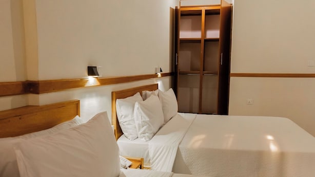 A hotel room with two beds, wooden headboards, white bedding, and a wooden wardrobe with a mirror. - Amakuza Residence (Kigali)