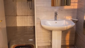 A bathroom with a shower, a sink, and a small wooden stool. - Amakuza Residence (Kigali)