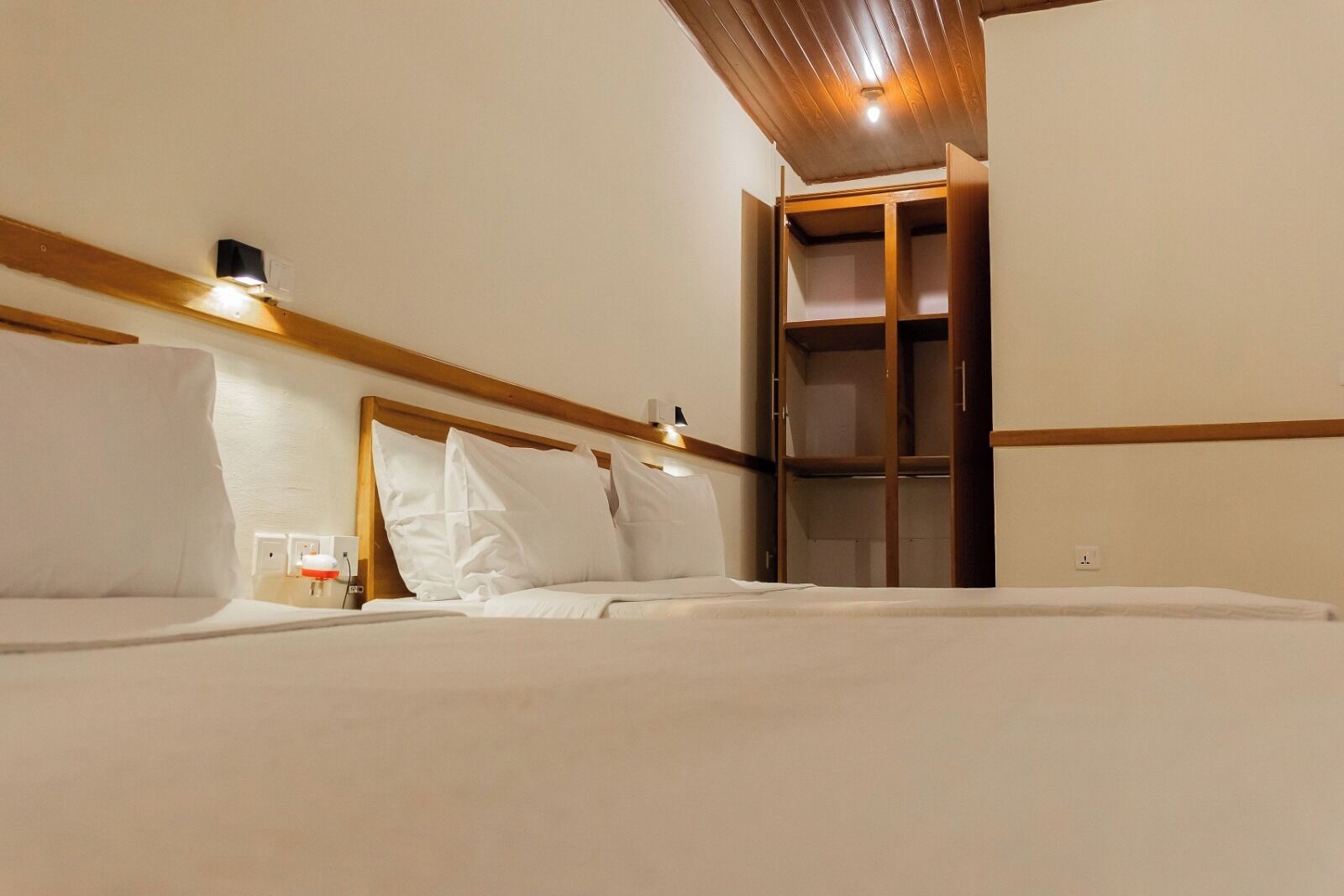 Une chambre d’hôtel avec une tête de lit en bois, un lit avec du linge de maison blanc, une table de chevet avec une lampe et une armoire avec un miroir.