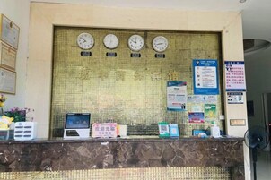 Una mesa de recepción con relojes, carteles informativos y un ordenador portátil.