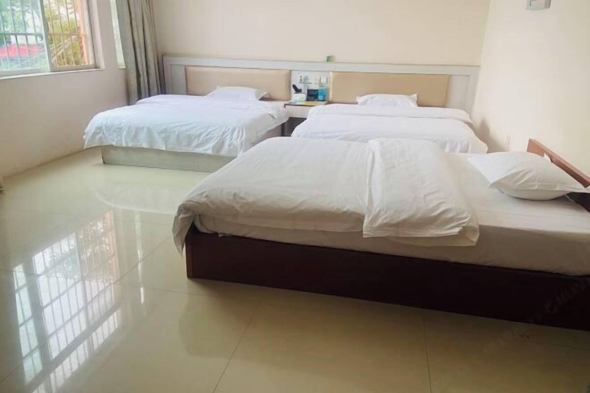 A hotel room with two beds, a bedside table with a lamp, and a window with curtains.