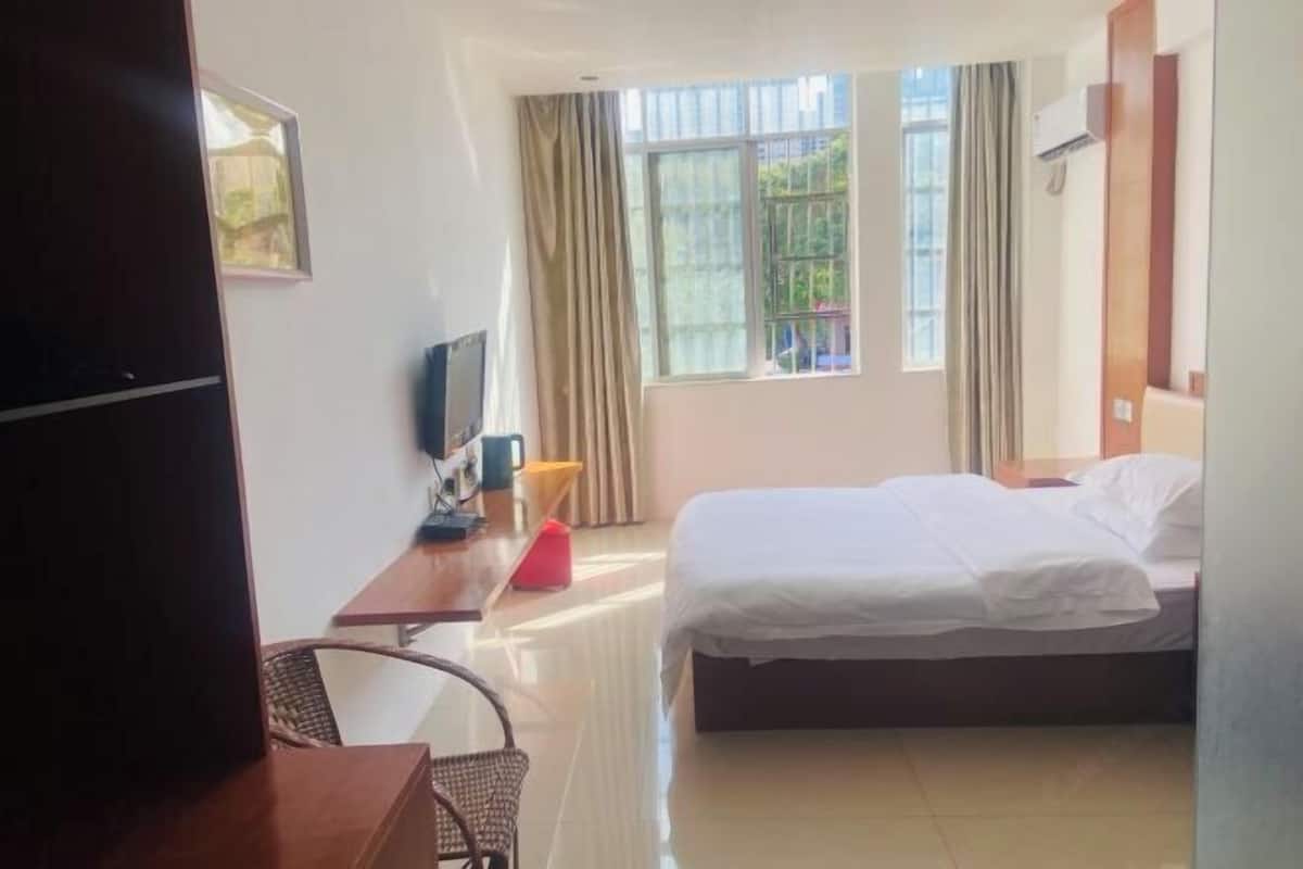 A hotel room with a bed, a desk, a chair, a TV, and a window with curtains.
