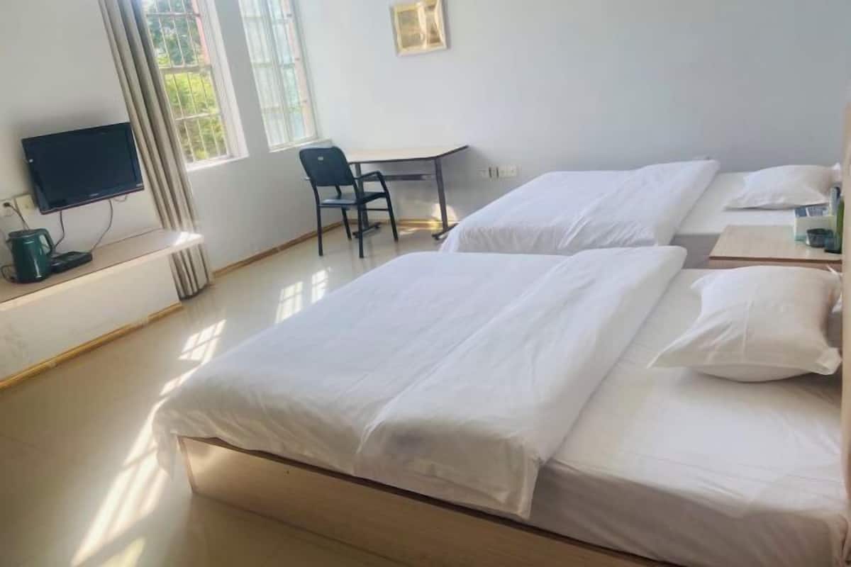 A hotel room with two beds, a desk, a chair, a television, and a window.