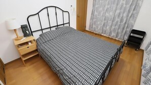 Ein Einzelbett mit schwarzem Metallgestell, ein Nachttisch aus Holz mit Schubladen, eine weiße Lampe und eine zudeckende Bettwäsche mit Muster.