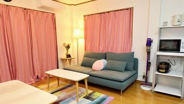 Ein Wohnzimmer mit einer Couch, einem kleinen Tisch, einer Lampe und einer Mikrowelle auf einem Regal.