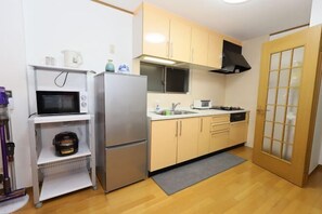 A compact kitchen with a microwave, refrigerator, sink, and wooden cabinets. - Guest House Kubo Homes Matsu (Osaka)