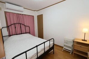 A single bed with a metal frame, a bedside table with a lamp, and a small white storage unit. - Guest House Kubo Homes Matsu (Osaka)