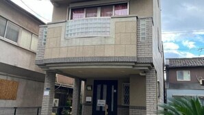 Ein zweistöckiges Gebäude mit Balkon, einer Tür mit Schild und einem Fenster mit Gittermuster.