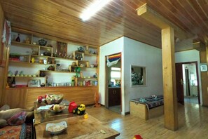 A spacious living room with wooden floors, a sofa, a coffee table with toys, and a bookshelf filled with various items. - Daocheng Snowberg Inn (Daocheng County)