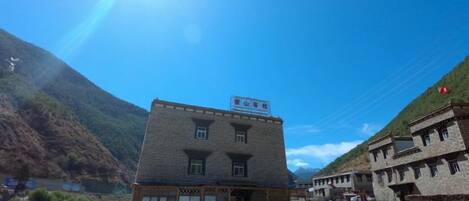 Un edificio con techo plano y un cartel, rodeado por una zona de grava y un paisaje montañoso.