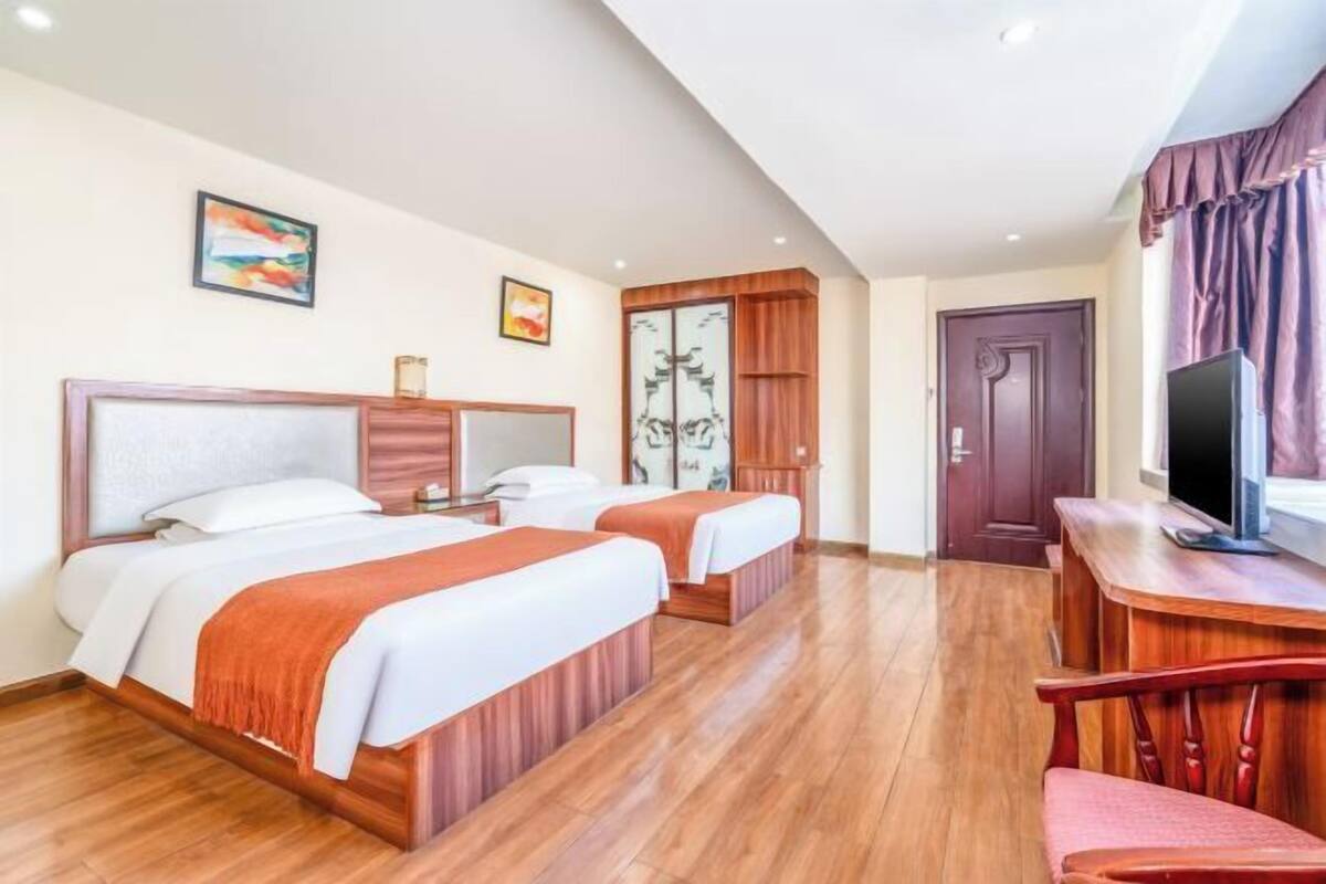 Ein Hotelzimmer mit zwei Betten, Holzboden, einem Fernseher und einem Schreibtisch.