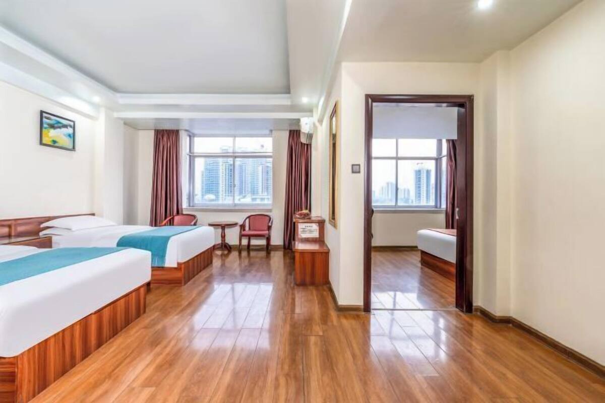 Ein Hotelzimmer mit zwei Betten, einem kleinen Tisch, einem Sessel und Blick auf die Stadt.
