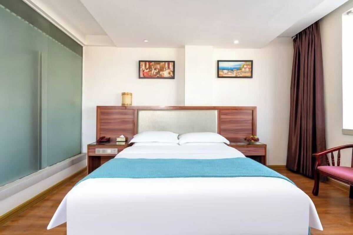Ein Hotelzimmer mit einem großen Bett, einem Nachttisch, einem Sessel und zwei gerahmten Bildern an der Wand.