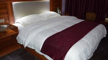 A hotel room with a large bed, wooden headboard, and a nightstand with a phone and bottle.