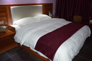 A hotel room with a large bed, wooden headboard, and a nightstand with a phone and bottle. - Lingshan Yincheng Business Hotel (Lingshan)