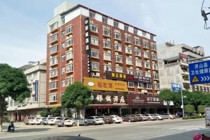 A multi-story hotel with a row of windows on the facade, a ground-level restaurant, and a parking lot with cars.