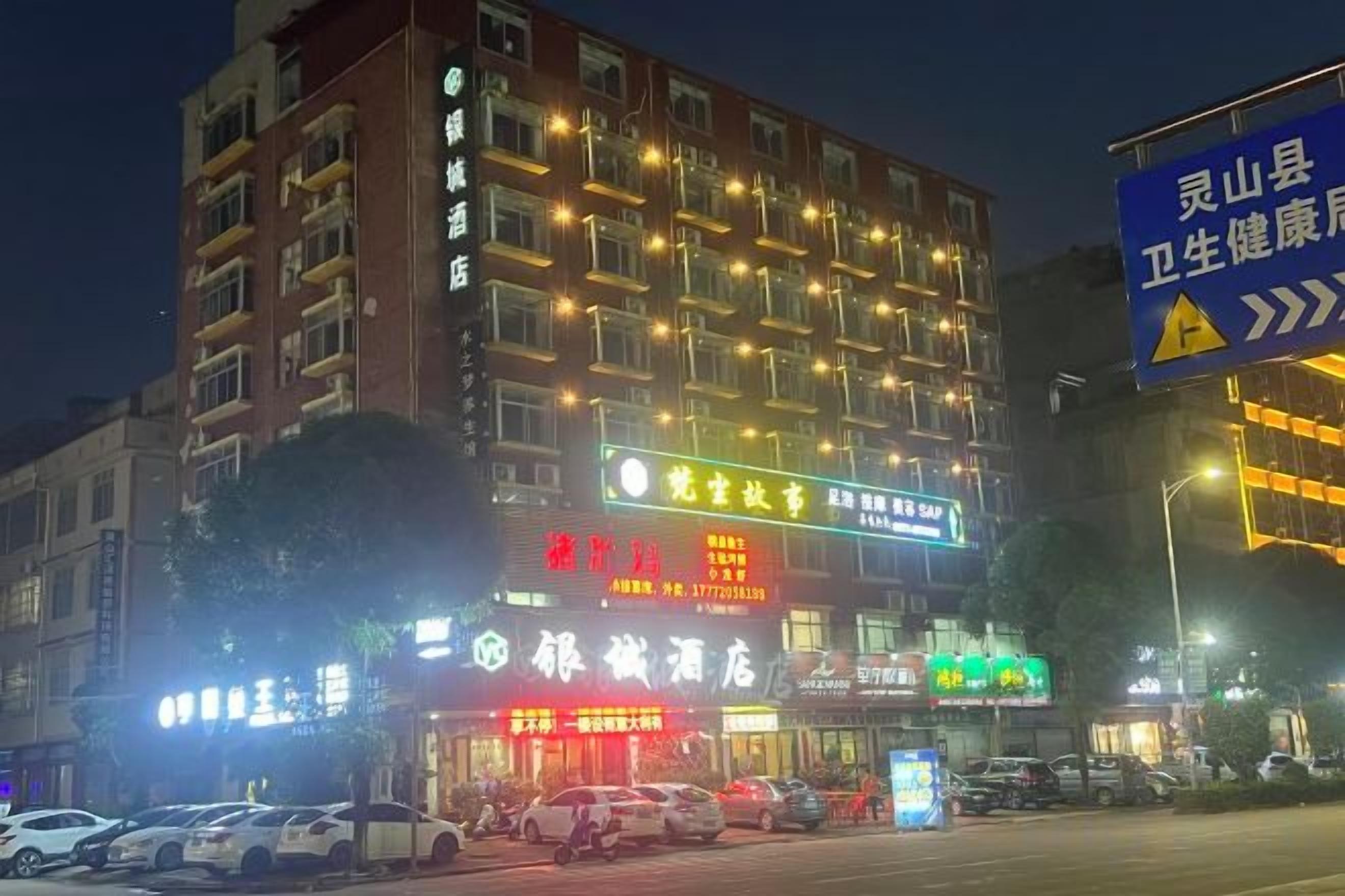A multi-story hotel with illuminated signage, a parking lot, and a street view.