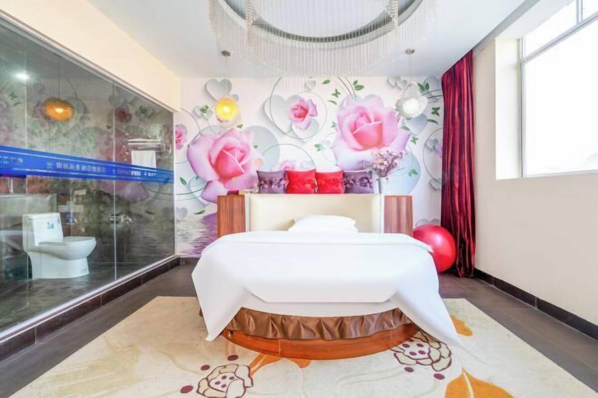Ein modernes Hotelzimmer mit einem großen Bett, einer Trennwand aus Glas und dekorativer Blumenkunst an der Wand.