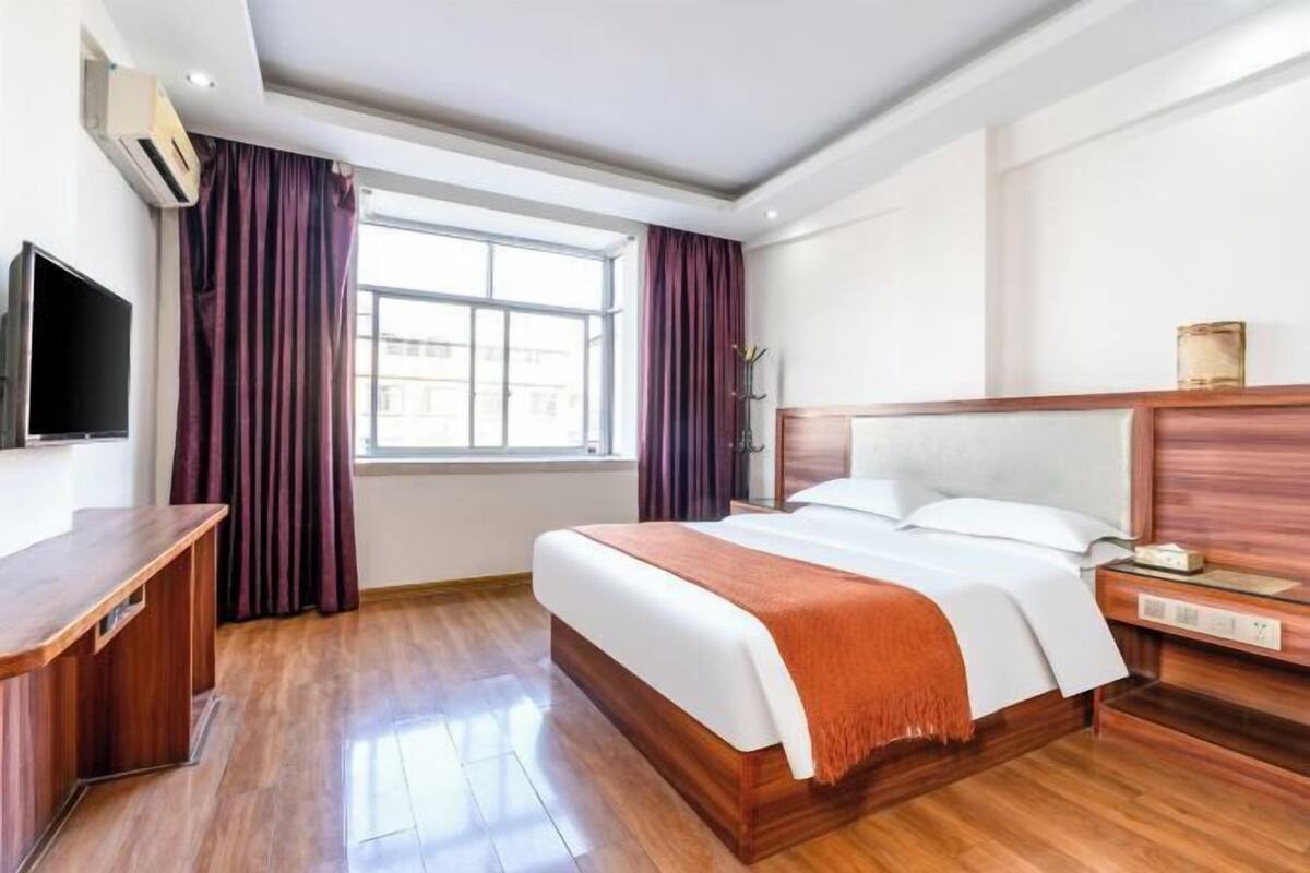 Ein Hotelzimmer mit einem Holzbett, einem Nachttisch, einem Fernseher und einem Fenster mit Vorhängen.