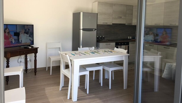 A modern kitchen with a built-in refrigerator and stove, a dining area with a white table and chairs, and a television on a wooden stand. - New Panoramic Villino in Porto Palo di Menfi Blue Flag ideal for families  (Menfi)