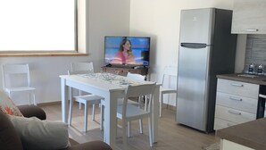 A modern living room with a sofa, dining table, chairs, a TV, and a kitchen area with a refrigerator and cabinets. - New Panoramic Villino in Porto Palo di Menfi Blue Flag ideal for families  (Menfi)