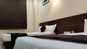 A hotel room with two beds, a dark headboard, white bedding, and a wall-mounted light fixture. - Hotel Kawa (Jaipur)