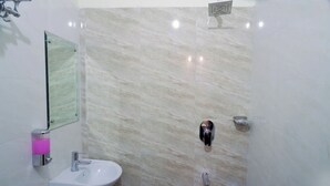 A bathroom with a marble wall, a sink, a mirror, and a shower. - Hotel Kawa (Jaipur)