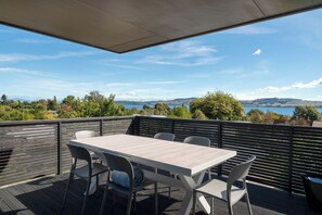 Eine Außenterrasse mit Tisch und Stühlen, mit Blick auf eine malerische Landschaft mit Hügeln und einem Gewässer.