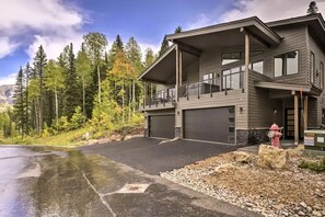 A modern two-story house with a garage, a balcony, and a driveway leading to a mountain view.
