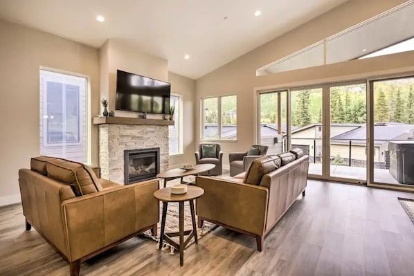 A spacious living room with a fireplace, comfortable seating, and large windows offering a view of the outdoors.