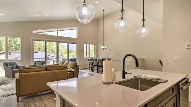 Une cuisine moderne dotée d’un grand îlot central, de luminaires suspendus et offrant une vue sur l’extérieur.