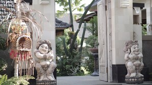 A traditional gate with statues, a decorative birdhouse, and lush greenery. - Green D'mel Bali (Nusa Dua)
