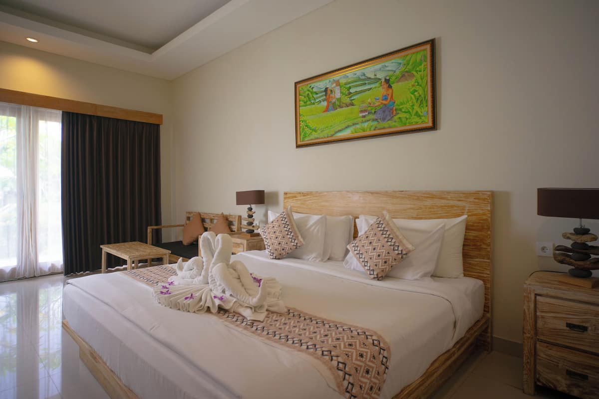 A hotel room with a large bed, a painting on the wall, and a view of the outdoors through the window.