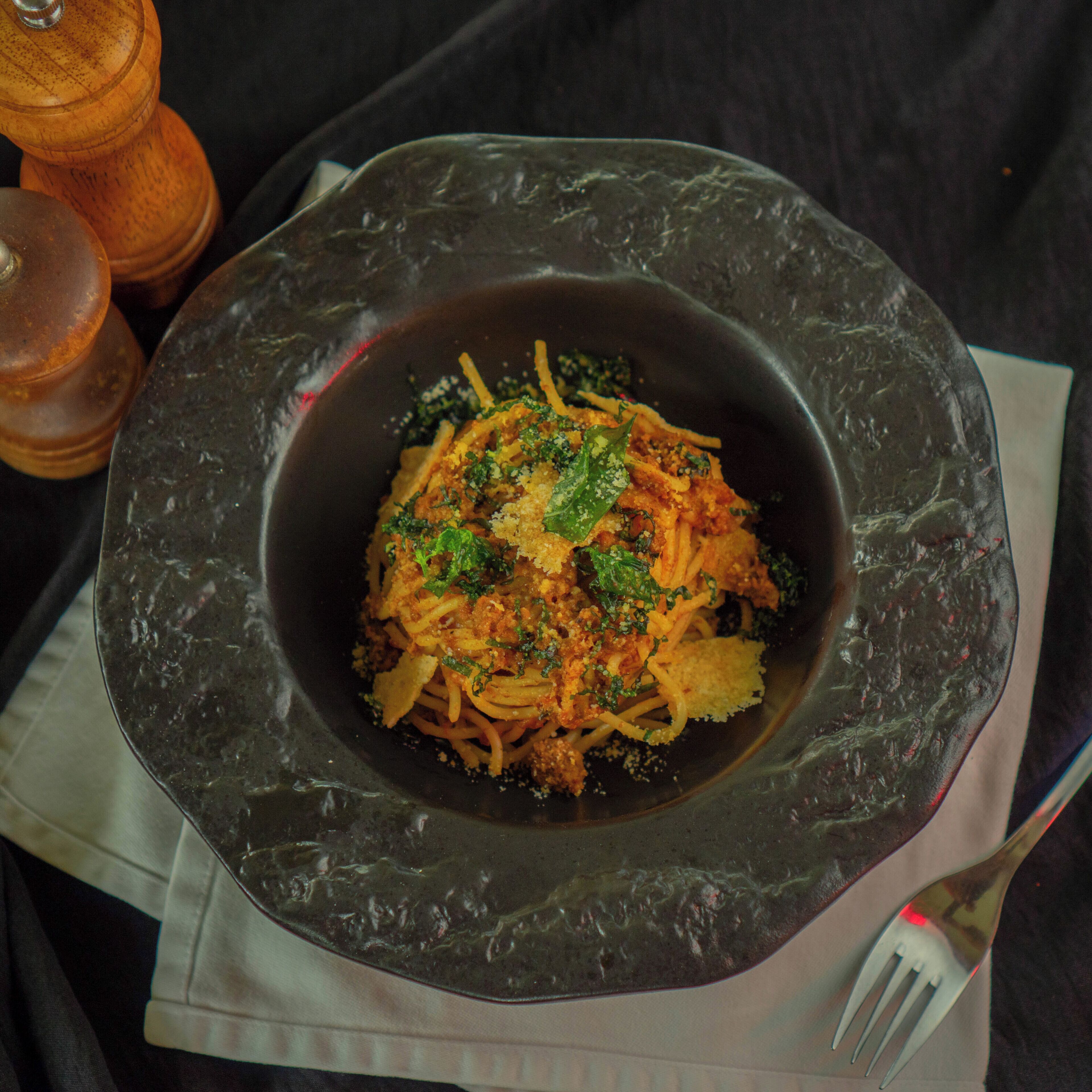A bowl of pasta with a dark, textured bowl on a table.