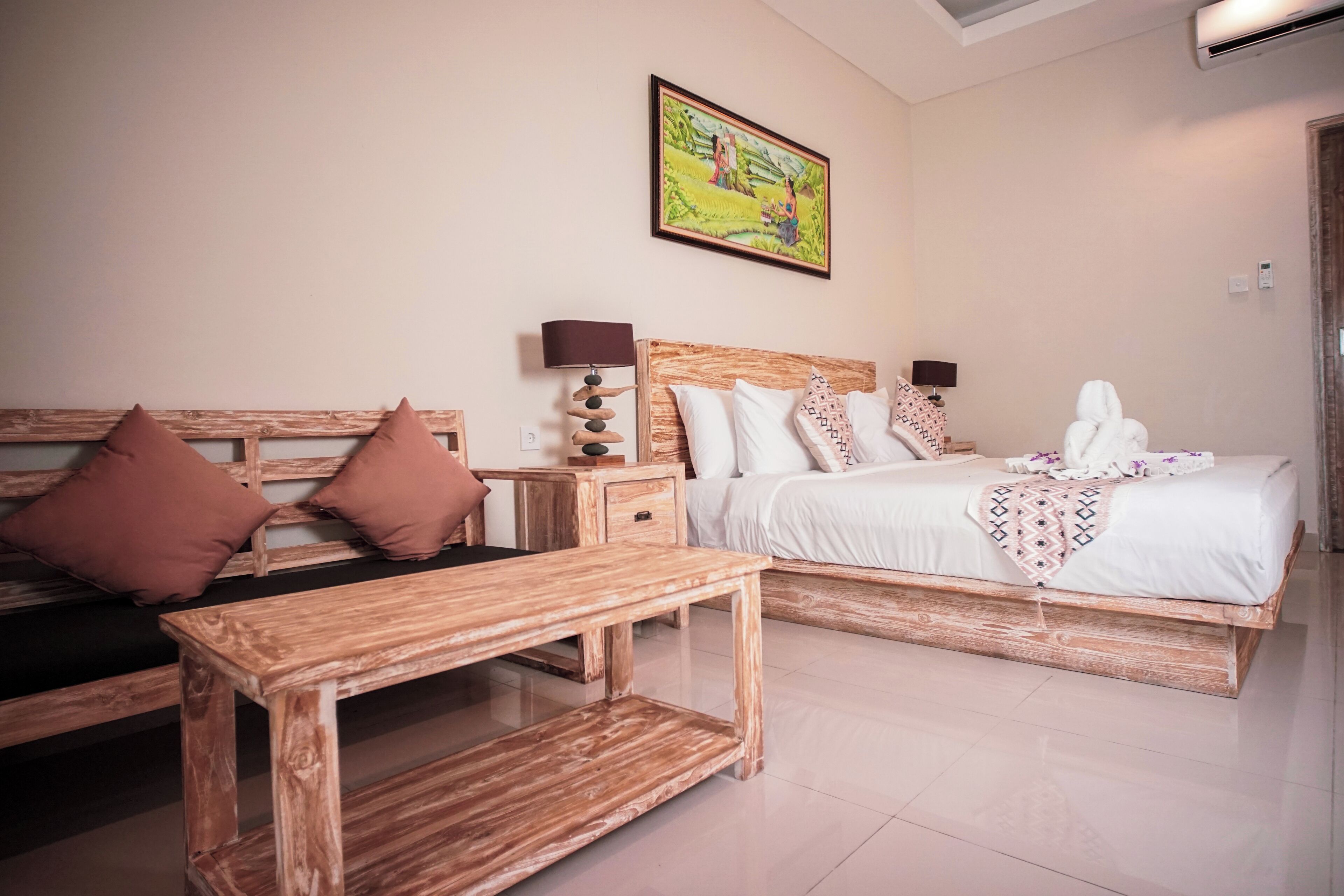 A hotel room with a wooden bed, a wooden bench, a nightstand with a lamp, and a painting on the wall.