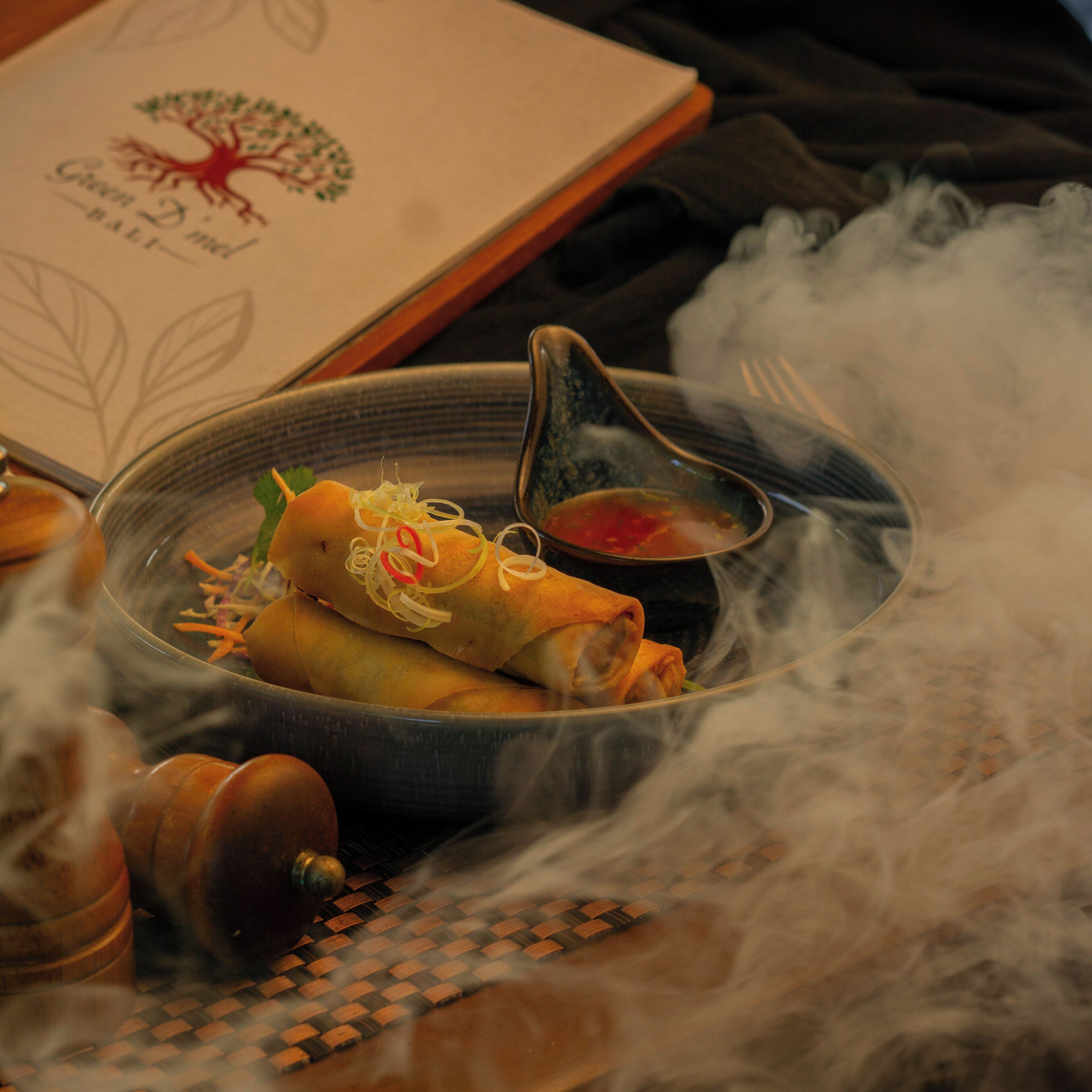 Un plato de comida con salsa, vapor y un libro de fondo.