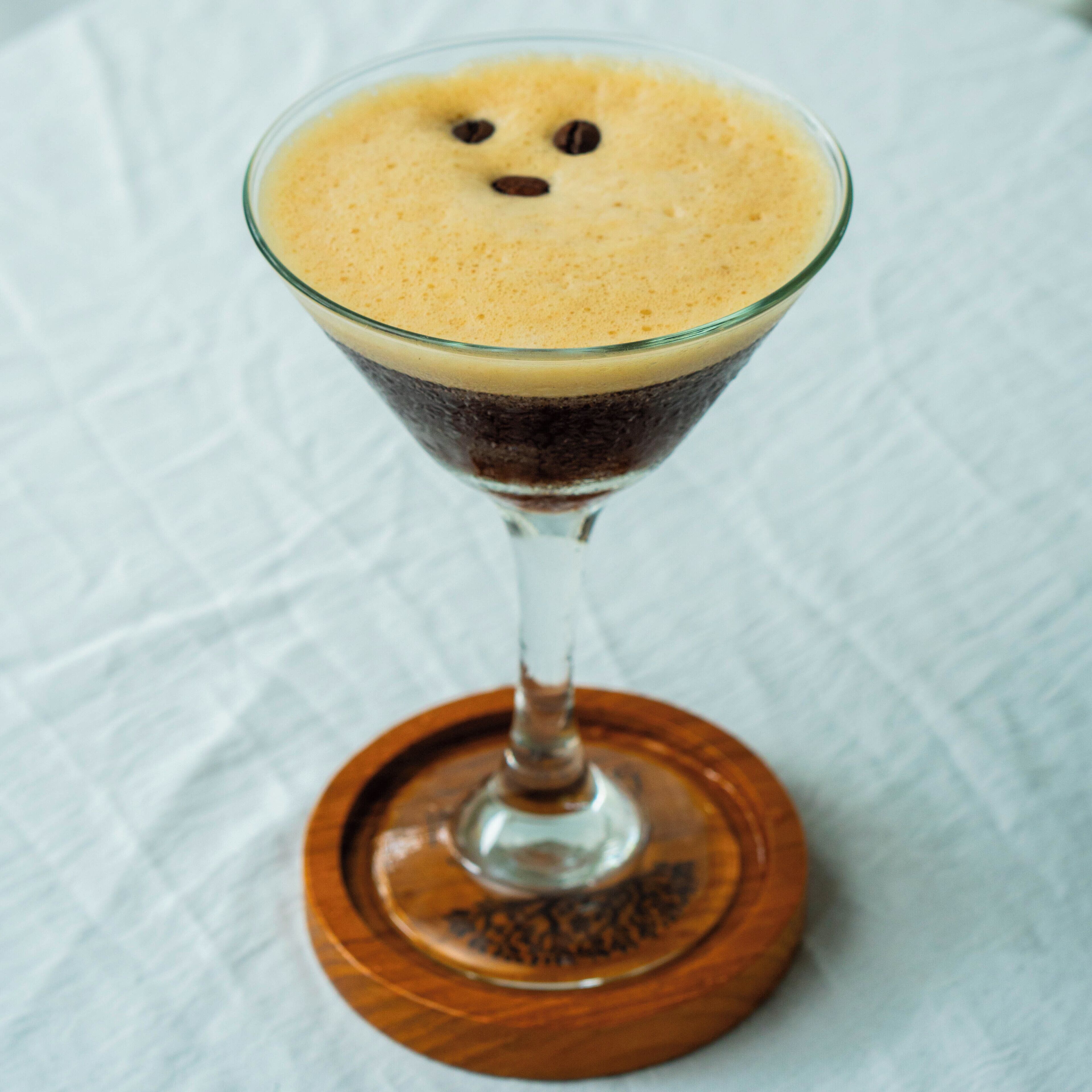 Ein Getränk in mehreren Schichten in einem Martini-Glas auf einem Holzteller.