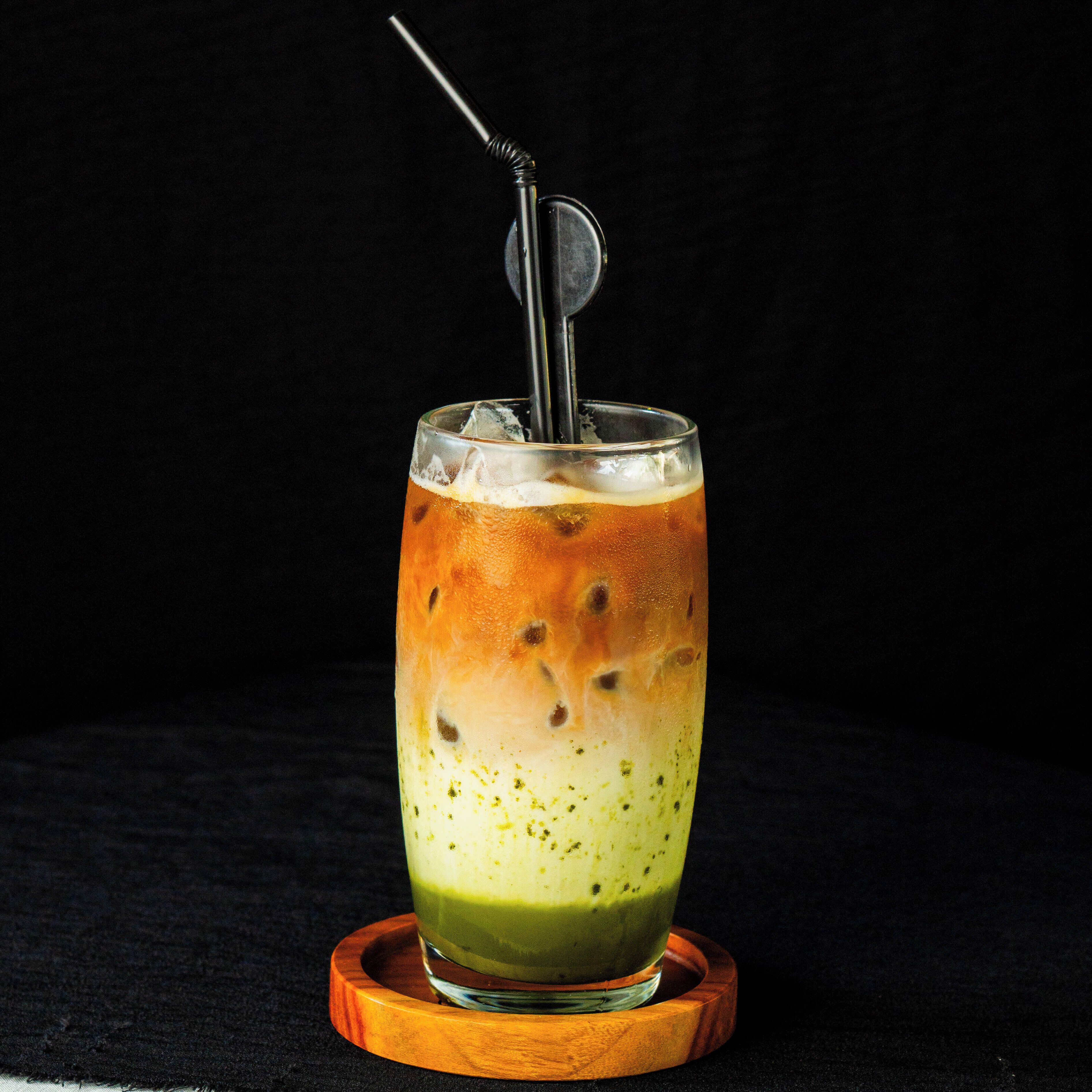 A glass of iced tea with a straw and a metal stirrer.