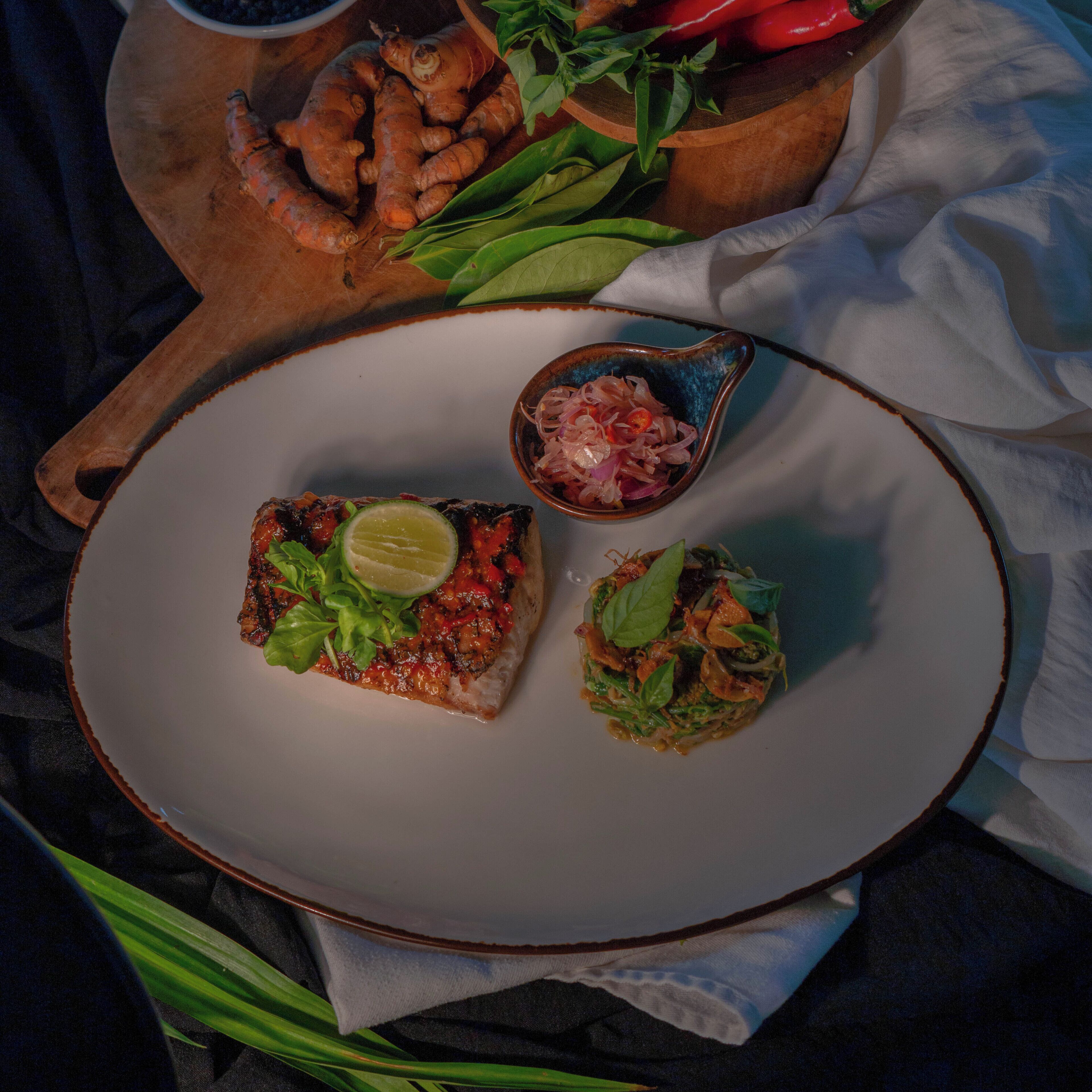 A plate with two dishes, a bowl of onions, and a wooden board with vegetables.
