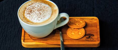 A white cup of coffee with a spoon on a wooden board with two cookies.