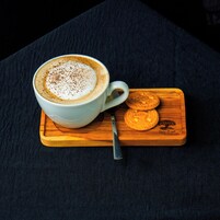 Eine weiße Kaffeetasse mit Löffel auf einer Holzbrettchen mit zwei Keksen.